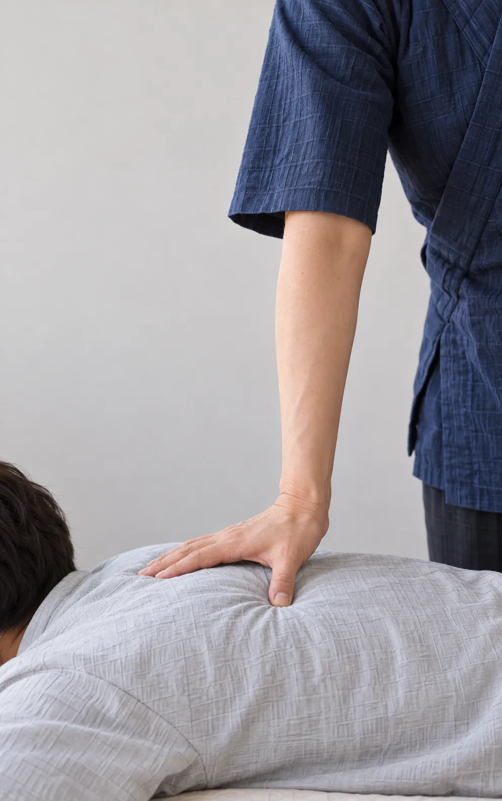 院長が肘を伸ばして横になった方の背の 1 点に親指の先を置き、肩から体の重みを下ろしている写真。ほかの指は背に添えている
